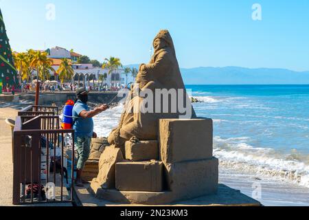 Ein Künstler spritzt Wasser auf eine Sandstatue am Strand von Olas Altas Playa del Muerto im Küstenort Malecon in Puerto Vallarta, Mexiko. Stockfoto