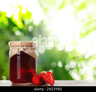 Ein Glas mit leckeren eingelegten Erdbeeren auf einem Holztisch vor einem verschwommenen grünen Hintergrund. Platz für Text Stockfoto