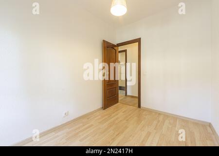 Leerer Raum mit lackierter Sapele-Holztür, Deckenleuchte und Laminatboden Stockfoto