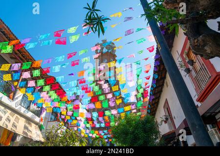 Blick auf die Kirche unserer Lieben Frau von Guadalupe mit bunten Flaggen auf der anderen Straßenseite an einem sonnigen Morgen in Puerto Vallarta Mexiko. Stockfoto