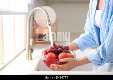 Eine Frau wäscht frische Trauben und Nektarinen in der Küchenspüle Stockfoto