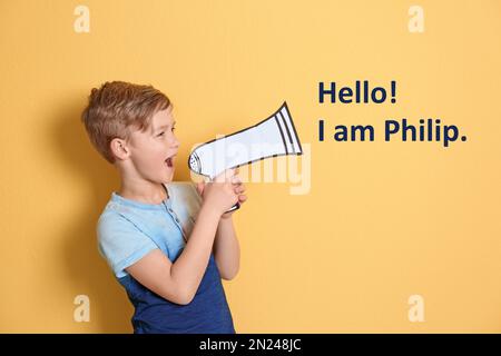 Süßer kleiner Junge, der Hallo sagt! Ich bin Philip und benutze ein Megafon aus Papier auf gelbem Hintergrund Stockfoto