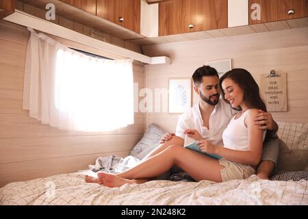 Glückliches junges Paar, das Buch auf dem Bett im Wohnwagen liest, Platz für Text. Campingurlaub Stockfoto