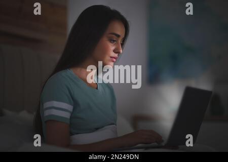 Junge Frau mit Nomophobie, die nachts einen Laptop im Bett benutzt. Insomnie-Konzept Stockfoto