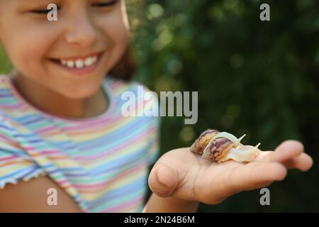 Mädchen, die draußen mit süßen Schnecken spielt, konzentrieren sich auf die Hand. Das Kind verbringt Zeit in der Natur Stockfoto