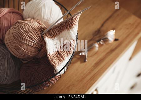 Garnknäuel und Stricknadeln in einem Metallkorb auf einem Holztisch, Nahaufnahme mit Platz für Text. Kreatives Hobby Stockfoto