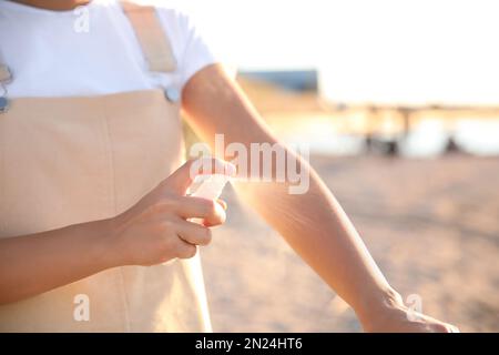 Junge Frau, die Insektenschutzmittel am Strand benutzt, Nahaufnahme Stockfoto