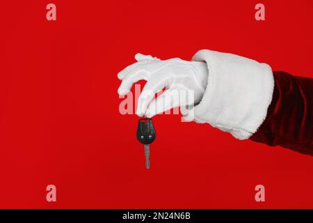 Der Weihnachtsmann hält den Autoschlüssel auf rotem Hintergrund, Nahaufnahme der Hand Stockfoto