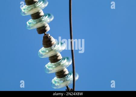 Glasisolatoren Elektrodraht Nahaufnahme. Details der Hochspannungsleitung mit blauem Himmelshintergrund Stockfoto