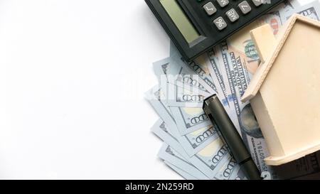 Ein Taschenrechner, Stift und Hausmodell auf einem Dollar-Geld oder auf Bankscheinen auf weißem Hintergrund mit Kopierbereich. Stockfoto