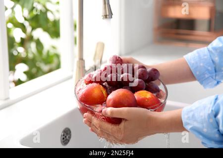 Eine Frau wäscht frische Trauben und Nektarinen in der Küchenspüle Stockfoto