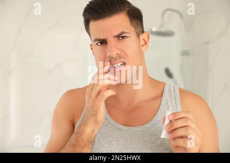 Emotionaler Mann mit Herpes, der Creme auf Lippen im Bad aufträgt Stockfoto