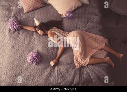 Erschöpfte Frau in festlichem Outfit, die zu Hause nach der Party im Bett schläft, über der Aussicht Stockfoto