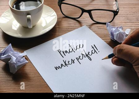 Ein Satz mit der Hand " Übung macht den Meister " zusammen mit Gläsern, Papierkorb und einer Tasse Kaffee auf einem hölzernen Hintergrund. Stockfoto