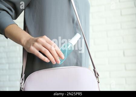 Frau, die Handdesinfektionsmittel in Handtasche steckt, drinnen, Nahaufnahme. Persönliche Hygiene während der COVID-19-Pandemie Stockfoto