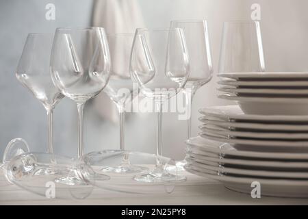 Set aus sauberem Geschirr und Weingläsern auf weißem Tisch im Innenbereich Stockfoto