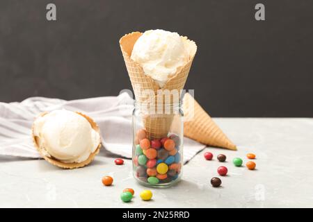 Köstliches Vanilleeis in Waffel mit Süßigkeiten auf hellgrauem Tisch Stockfoto