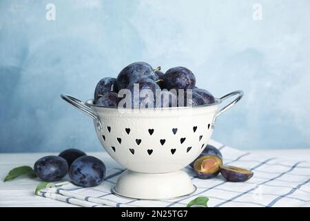 Köstliche reife Pflaumen im Sieb auf dem Tisch vor hellem Hintergrund Stockfoto