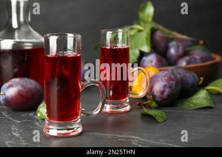 Köstlicher Pflaumenlikör und reife Früchte auf schwarzem Tisch. Hausgemachtes, starkes alkoholisches Getränk Stockfoto