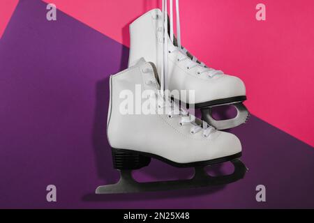 Ein Paar weiße Schlittschuhe, die auf einem farbigen Hintergrund hängen Stockfoto