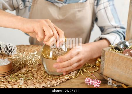 Frau, die Schneekugel am Holztisch macht, Nahaufnahme Stockfoto