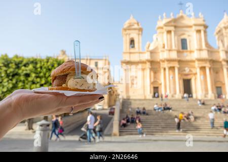 Nahaufnahme einer Hand mit einer Brioche mit Eis auf der Piazza del Duomo in Noto, Sizilien Stockfoto