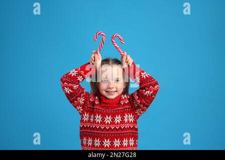 Süßes kleines Mädchen in gestricktem Weihnachts-Pullover mit Zuckerstangen auf blauem Hintergrund Stockfoto