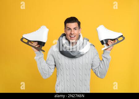 Emotionaler Mann mit Schlittschuhen auf gelbem Hintergrund Stockfoto