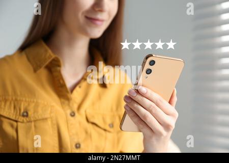 Frau, die ihre Rezension online über ein Smartphone im Haus verlässt, Nahaufnahme. Fünf Sterne über dem Gerät Stockfoto