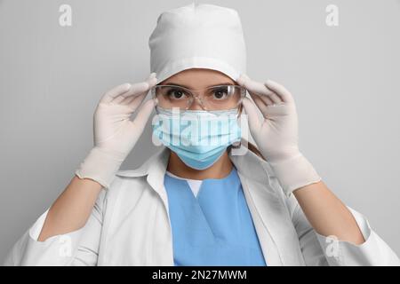 Arzt in Schutzmaske und medizinische Handschuhe Brille gegen hellgrauen Hintergrund aufsetzen Stockfoto