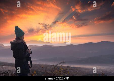 Wunderschöne junge Fotografin, die mit einer professionellen Kamera im Freien fotografiert. Stockfoto