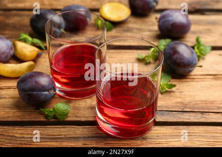 Köstlicher Pflaumenlikör, Minze und reife Früchte auf einem Holztisch. Hausgemachtes, starkes alkoholisches Getränk Stockfoto