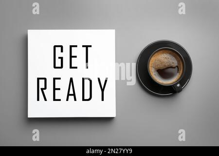 Karte mit Text „Get Ready“ und einer Tasse Kaffee auf einem hellgrauen Tisch, flach liegend Stockfoto