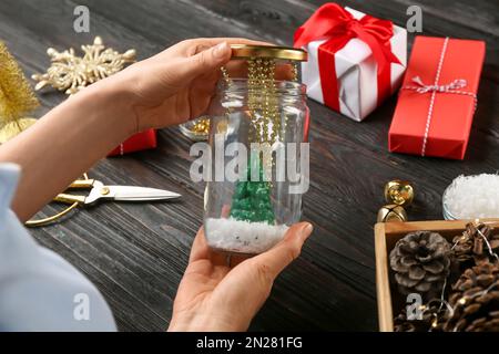 Frau, die Schneekugel am schwarzen Holztisch macht, Nahaufnahme Stockfoto