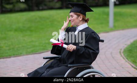 Eine weiße Frau im Rollstuhl hält ihr Diplom und weint vor Freude draußen. Stockfoto