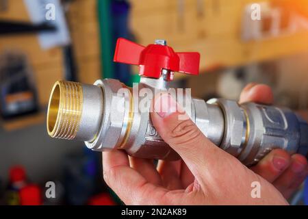 Ein Mann, der einen halbrotierenden Wasserhahn in der Hand hält. Auswahl des Hahns für die Wasserheizung am Rohr. Nahaufnahme... Stockfoto