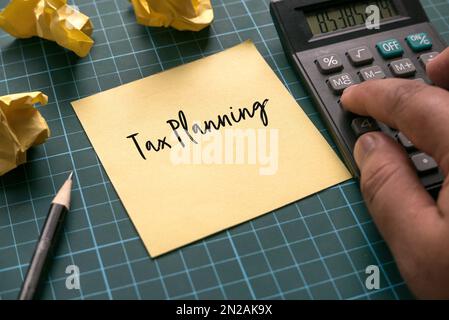 Ein Taschenrechner und ein gelber Notizzettel mit Steuerplanung auf einer grünen Handwerkmatte. Stockfoto