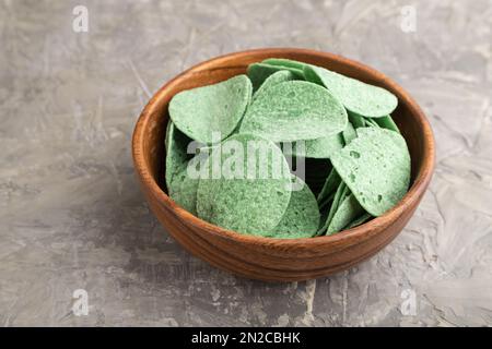 Grüne Kartoffelchips mit Kräutern in einer Holzschüssel auf grauem Betonhintergrund. Seitenansicht, Nahaufnahme. Stockfoto