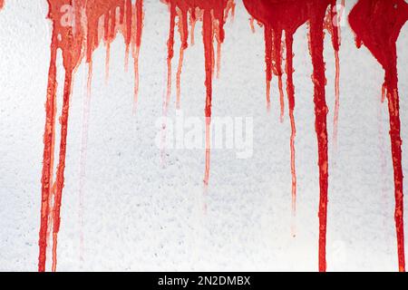 Rotes Blut an der Wand. Rote Farbe tropft an die graue Wand. Flecken von der Inschrift. Graffiti-Details. Stockfoto