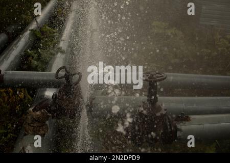 Wasser fließt aus dem gebrochenen Rohr. Durchbruch in der Pipeline. Unfall in der Kesselstation. Wasserfluss. Stockfoto