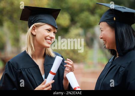 Wir haben endlich unseren Abschluss gemacht. Zwei junge College-Absolventen mit ihren Diplomen, während sie Mütze und Kleid tragen. Stockfoto