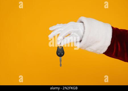 Der Weihnachtsmann hält den Autoschlüssel auf gelbem Hintergrund, Nahaufnahme der Hand Stockfoto
