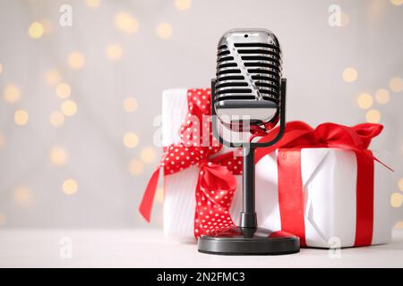 Retro-Mikrofon und Geschenkboxen auf dem Tisch gegen verschwommene Lichter, Platz für Text. Weihnachtsmusik Stockfoto