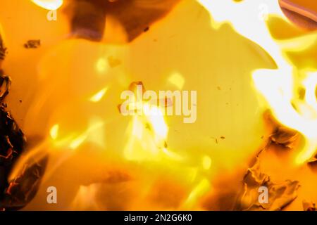 Flammen auf einem brennenden silbernen Kreuz, die in der Nacht glühen. Nahaufnahme brennendes Papier mit silbernem Kreuz in der Mitte auf schwarzem Hintergrund. Stockfoto