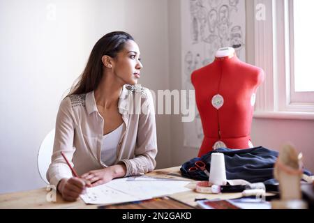 Neue Designs erfinden. Ein junger Modedesigner, der an ein paar Skizzen arbeitet. Stockfoto