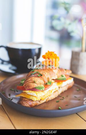 Croissant gefüllt mit Avocado, Tomaten und Ei auf einem Holztisch in einem Restaurant Stockfoto