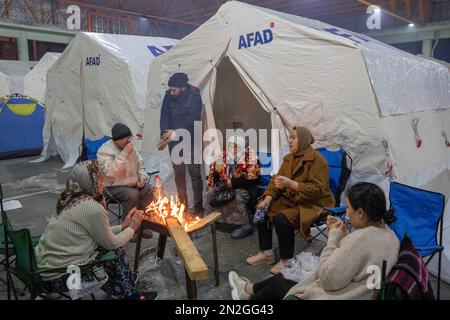 Adana, Türkei. 7. Februar 2023. Überlebende wärmen sich in der Nähe eines Feuers in einem Hilfszentrum in Adana. Die Such- und Rettungsbemühungen werden in einer Wohnung fortgesetzt, die bei dem Erdbeben am Morgen des 6. Februar 2023 in Adana, Türkei, zerstört wurde. Such- und Rettungsaktionen werden in den Trümmern von Gebäuden durchgeführt, die im zentralen Bezirk Cukurova von Adana aufgrund des Erdbebens der Stärke 7,7 zerstört wurden, dessen Epizentrum der Bezirk Pazarcik von Kahramanmaras ist und 10 Provinzen betrifft. (Kreditbild: © Tolga Ildun/ZUMA Press Wire) NUR REDAKTIONELLE VERWENDUNG! Nicht für den kommerziellen GEBRAUCH! Stockfoto