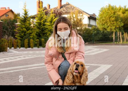 Frau in Schutzmaske mit englischem Cocker Spaniel draußen. Gehhund während der COVID-19-Pandemie Stockfoto