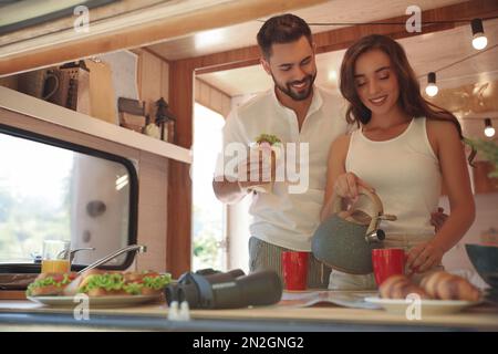 Glückliches junges Paar, das im Wohnwagen frühstückt. Campingurlaub Stockfoto