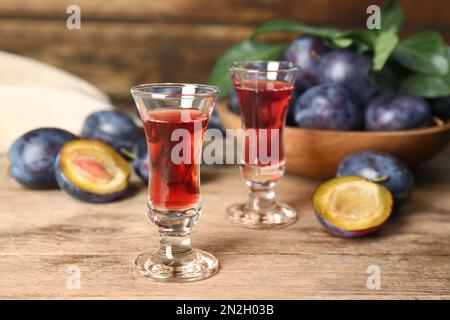 Köstlicher Pflaumenlikör und reife Früchte auf einem Holztisch. Hausgemachtes, starkes alkoholisches Getränk Stockfoto